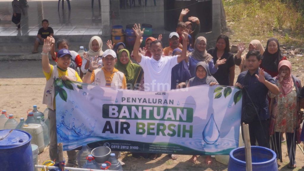 Sekelompok orang melambaikan tangan sambil memegang spanduk bertuliskan Penyaluran Bantuan Air Bersih